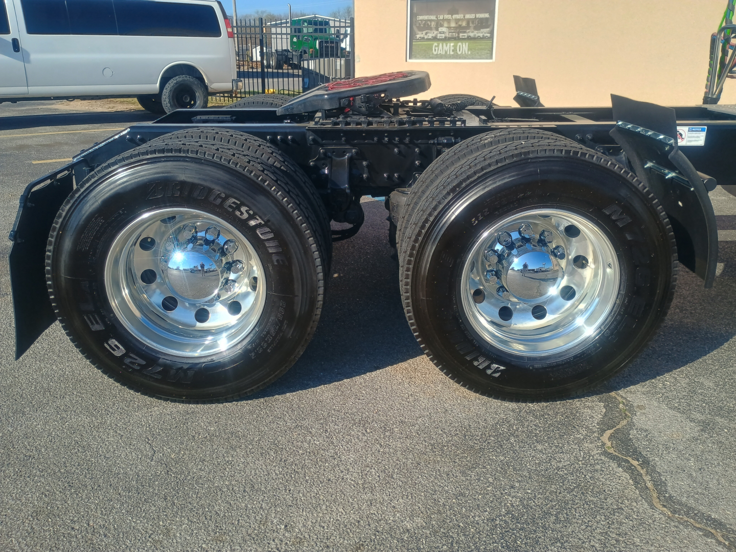 Dual rear truck wheels showing polished chrome rims and Bridgestone tires, part of a Mack AN64T64 chassis with fifth wheel and frame components visible.
