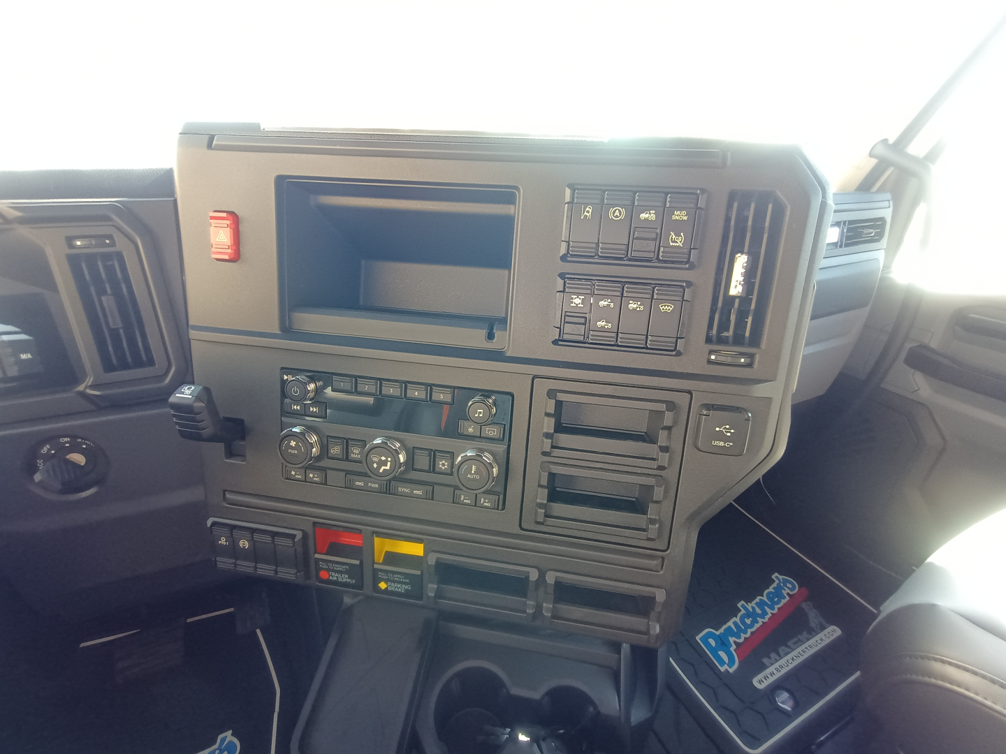 Dashboard of a Mack truck cab showing control panels, switches, and climate controls with a touchscreen slot and various labeled buttons.