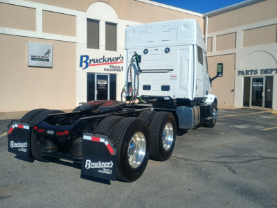 Truck chassis and cab of a 2027 Mack AN64T64 conventional sleeper, exposed rear dual-axle setup, white cab, at a dealership lot.