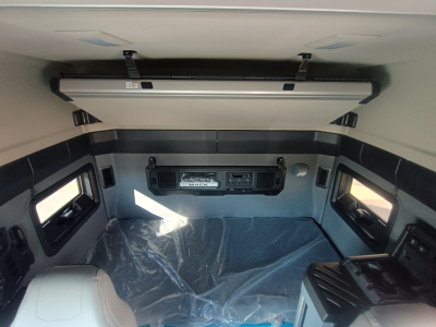Truck cab interior showing overhead bunk area and control panel with storage shelves.
