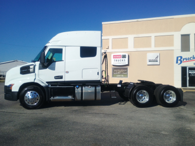 Truck side view showing 2027 Mack AN64T64 conventional sleeper chassis with white cab and dual rear axles, parking lot background.