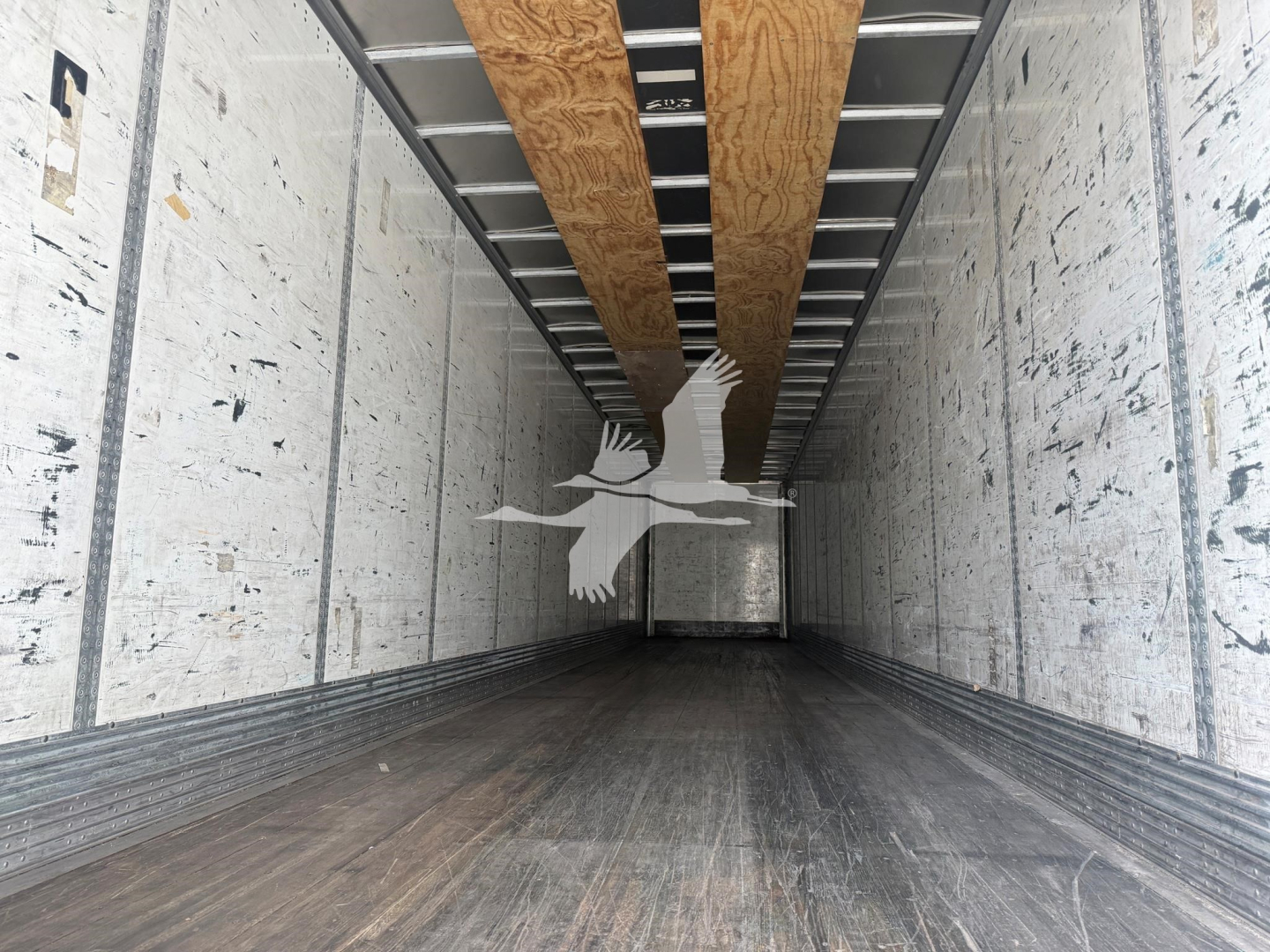 Trailer interior showing empty dry van with wooden floor beams and metal side walls.