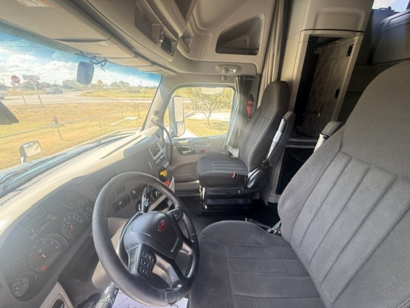 Peterbilt 579 cab interior showing steering wheel, metric gauges, driver's seat, and sleeper cabin doorway.