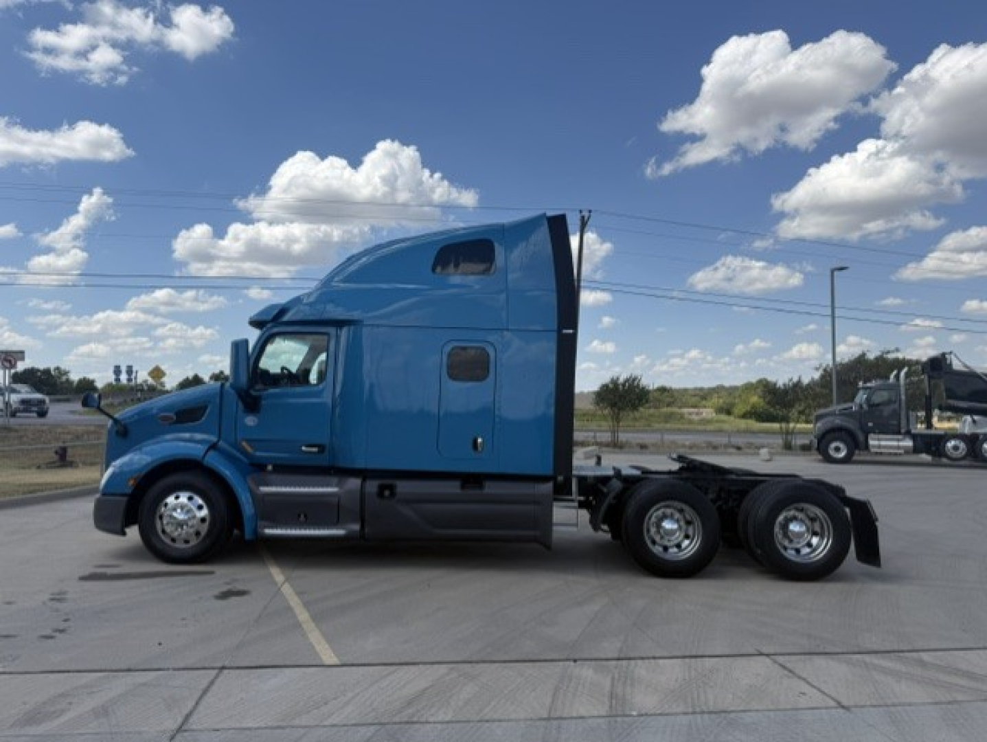 Peterbilt 579 conventional sleeper tractor in blue, side view, triple rear axles, cab elevated with aerodynamic sleeper, clear sky.