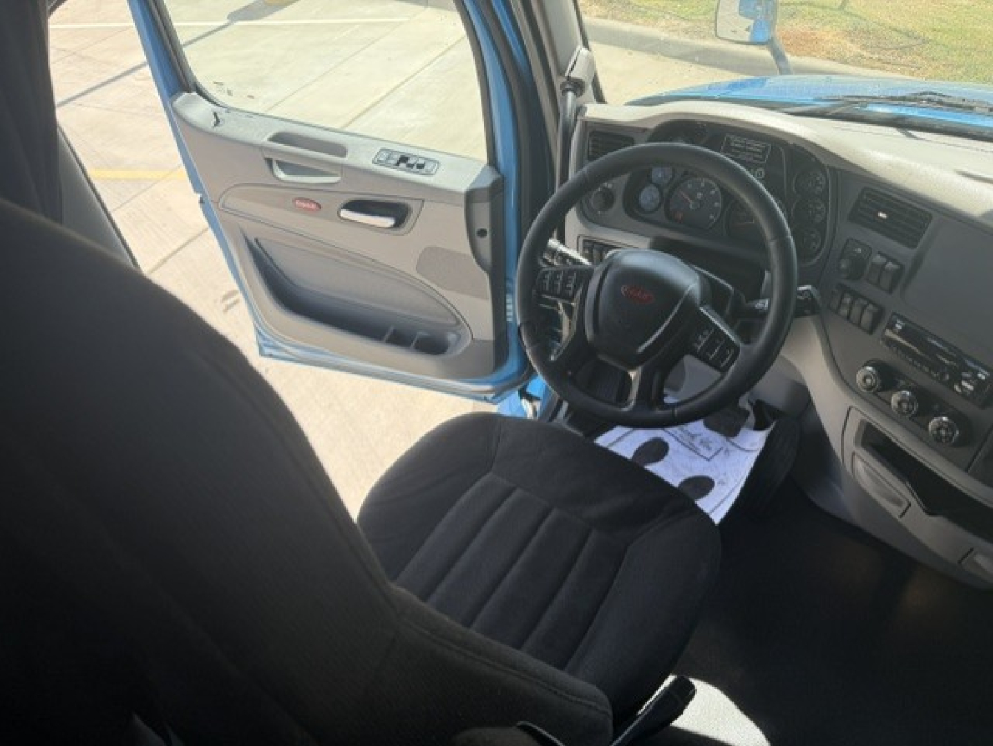 Interior view of a Peterbilt 579 with the driver door open, showing steering wheel, dashboard, and seating.