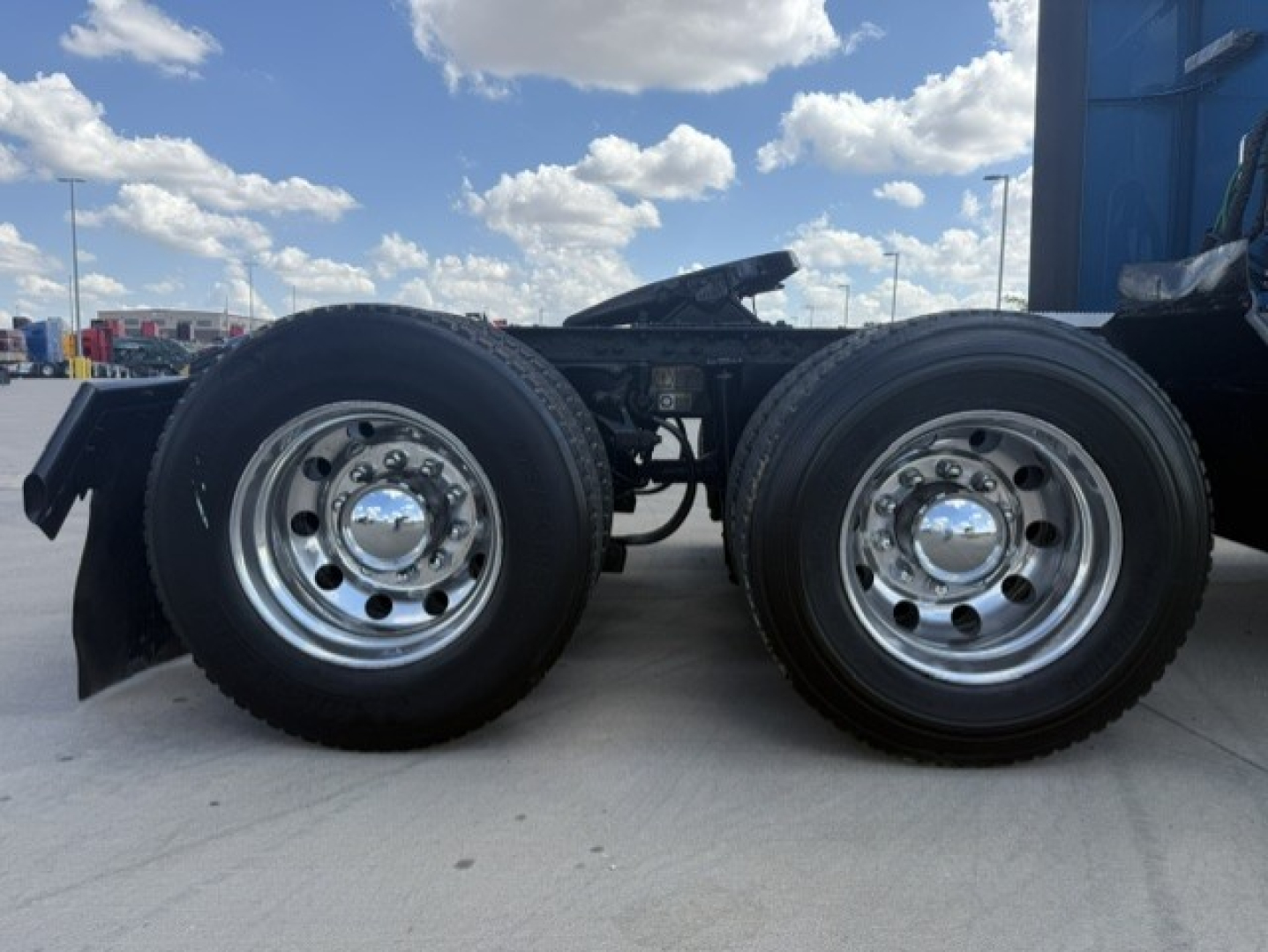 Peterbilt 579 tractor rear dual axles showing chrome wheel hubs and tires, part of truck chassis with blue sky background.