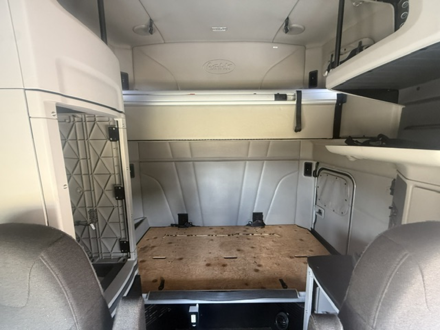 Peterbilt 579 sleeper cab interior cargo area with wood floor, storage compartments, and visible overhead rack; cab interior view from cab doorway.