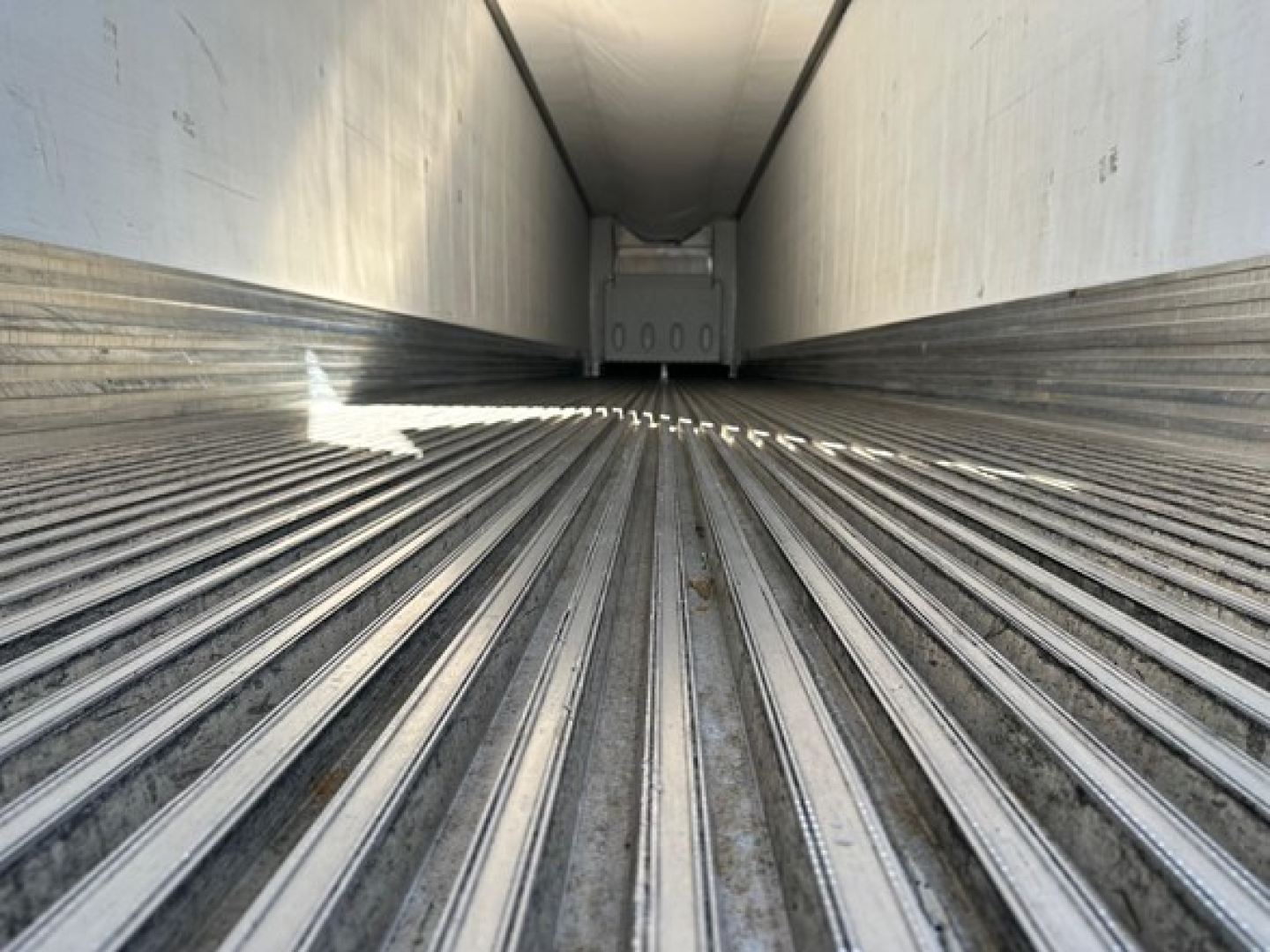 Trailer interior showing empty refrigerated trailer cargo area with ribbed metal floor and sidewalls, rear doors closed.