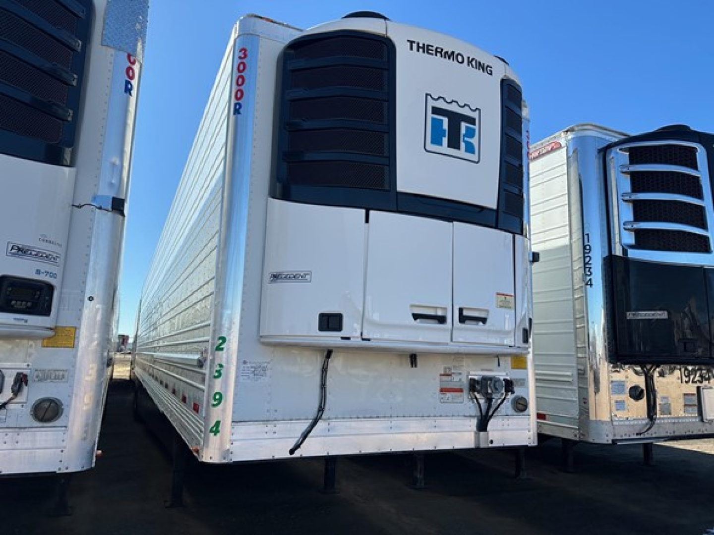 Trailer refrigeration unit on a Thermo King reefer trailer with white body and black vents, other trailers on either side.