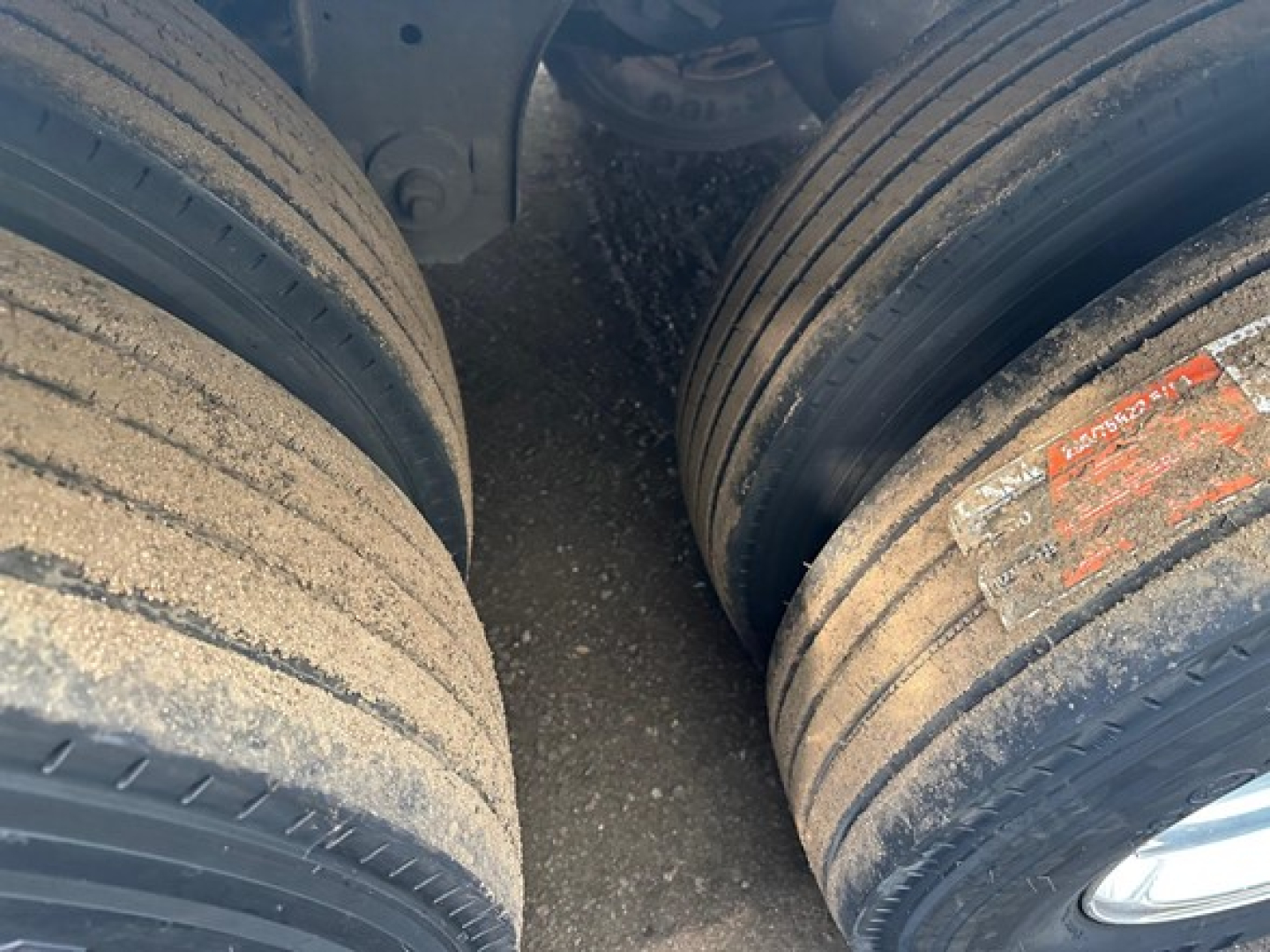 Close-up of a trailer rear dual tires with dirt and wear, showing sidewall treads and a red/orange label on the right tire.