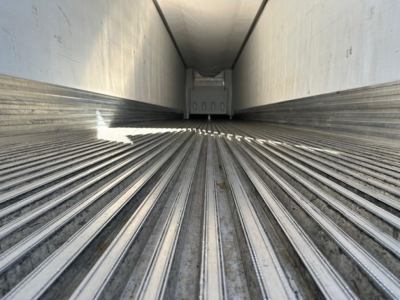 Trailer interior showing empty refrigerated trailer cargo area with ribbed metal floor and sidewalls, rear doors closed.
