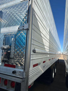 Trailer rear door with diamond plate pattern and reflective tape, side paneling, dual rear wheels, corner of a refrigerated trailer.