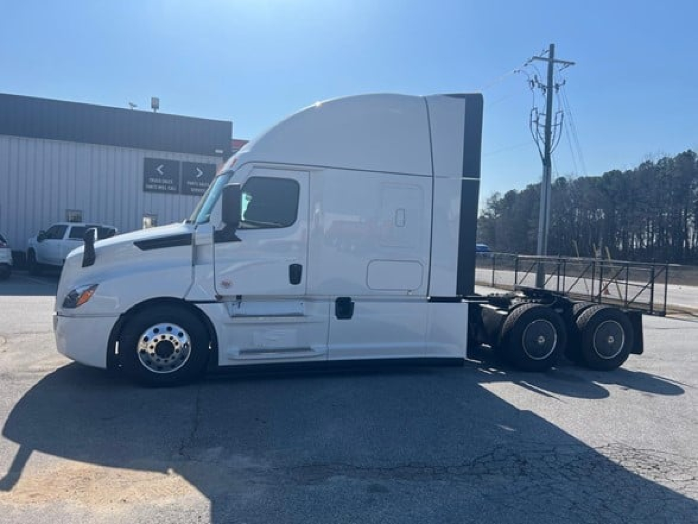 Truck side view of a white Freightliner Cascadia 126 tractor with aerodynamic sleeper cab, showing front wheel, side mirrors, and dual rear axles.