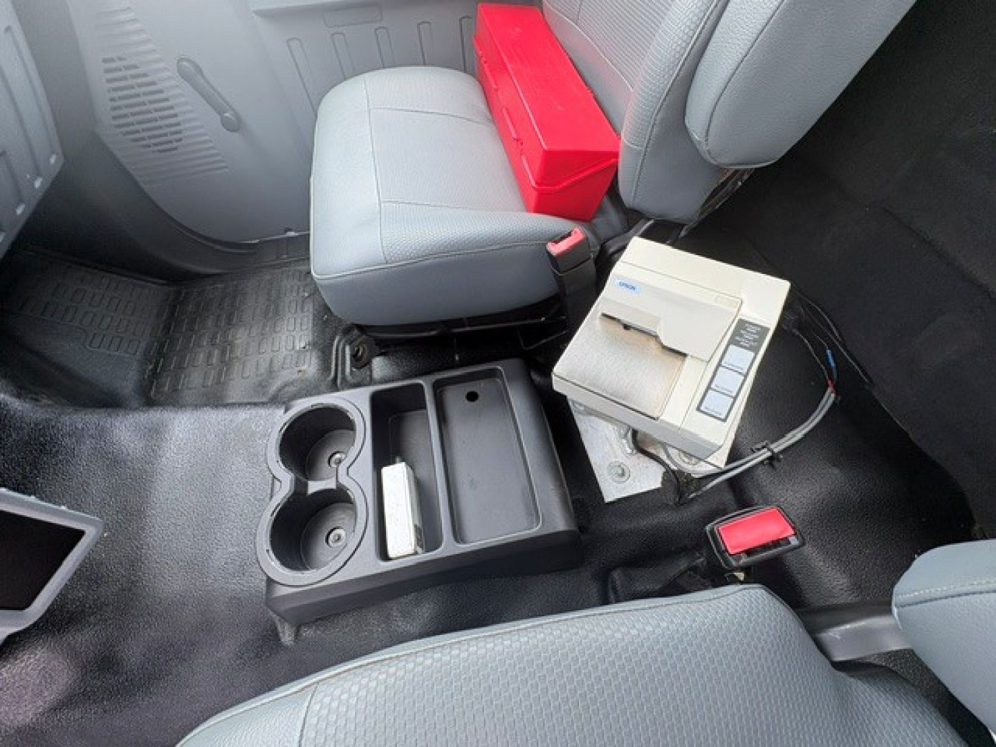 Cab interior of a 2016 Ford F-750 showing center console with cup holders, storage tray, red toolbox, and a digital control unit near the passenger seat.