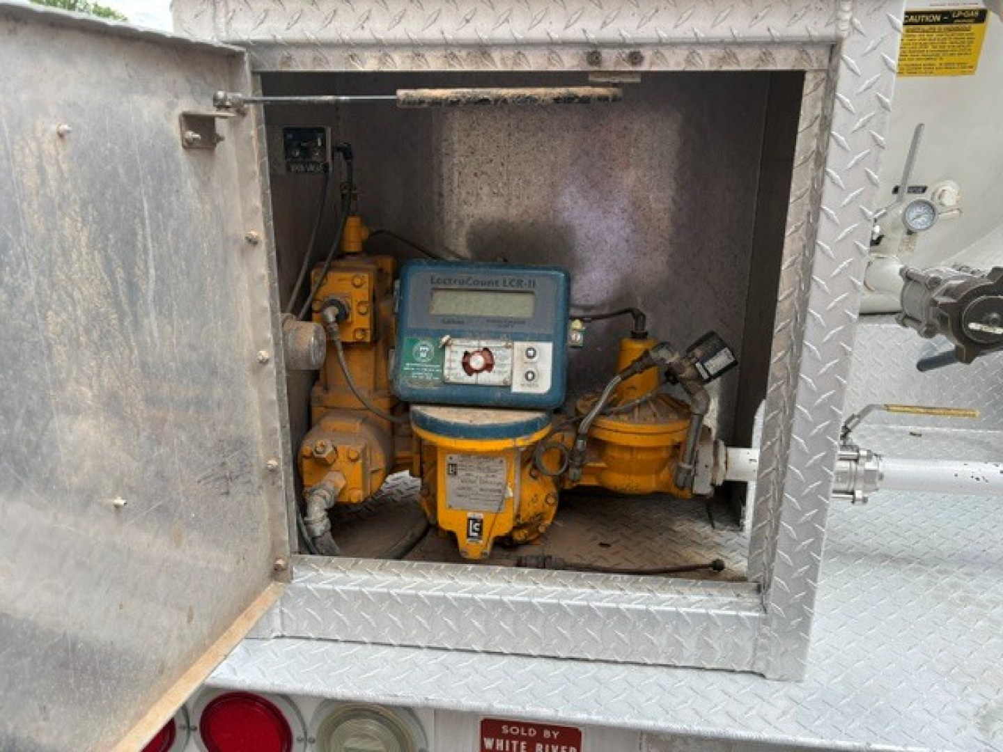 Gas engine-driven pump/gas meter inside square service hatch on a Ford F-750 truck with diamond plate exterior.