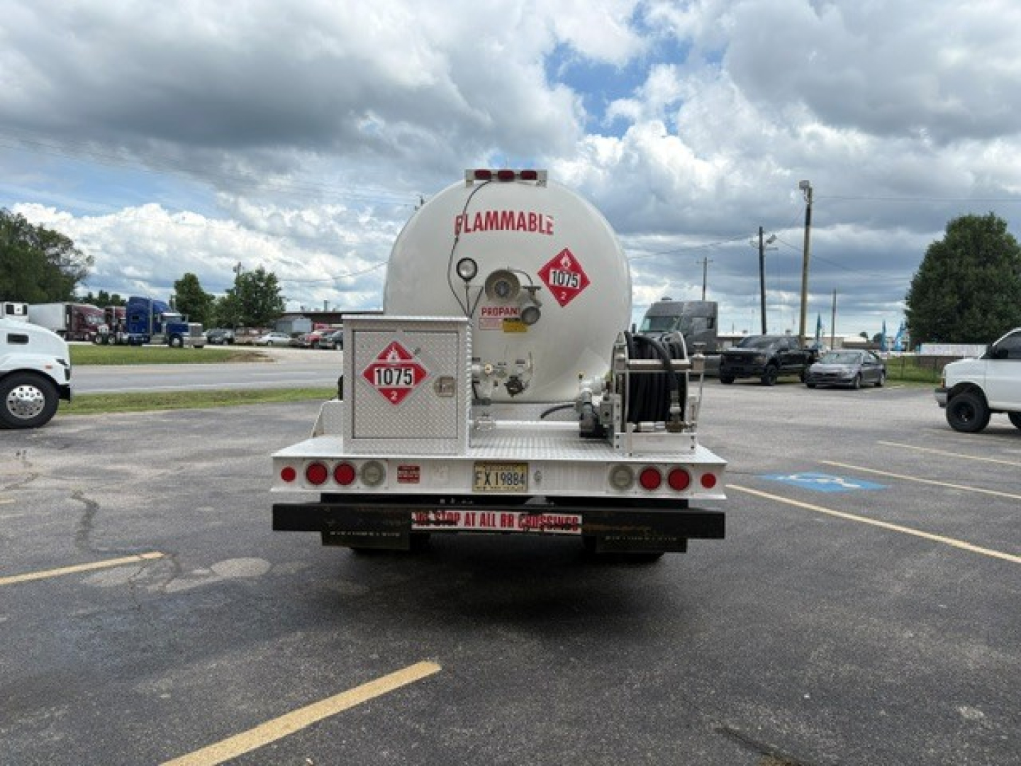 Rear view of a 2016 Ford F-750 truck with a large white cylindrical tank labeled FLAMMABLE and hazard placards. Trailer rear with bumper, lights, and spare equipment racks.