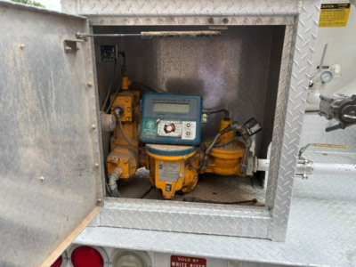 Gas engine-driven pump/gas meter inside square service hatch on a Ford F-750 truck with diamond plate exterior.