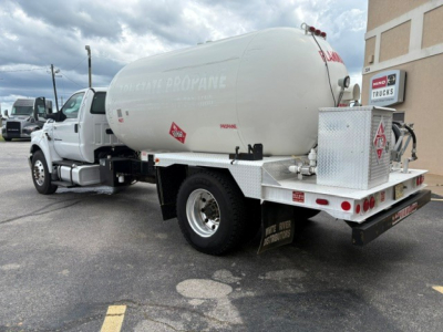 Ford F-750 utility truck with a cylindrical tank, rear platform, and fuel decals visible in a parking lot.