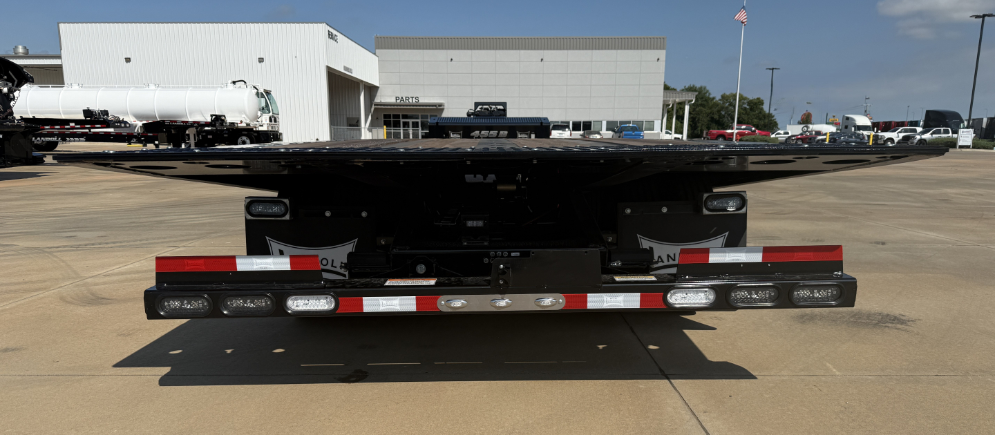 Lowboy trailer rear view with reflective tape and bumper lights, 55-ton traveling axle Landoll 455B-53 trailer, outdoor lot.
