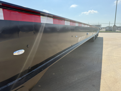 Lowboy trailer side showing reflective red-and-white stripes and black metal surface with bulbed reflectors along the side of a 2027 Landoll 455B-53 55-ton traveling axle trailer