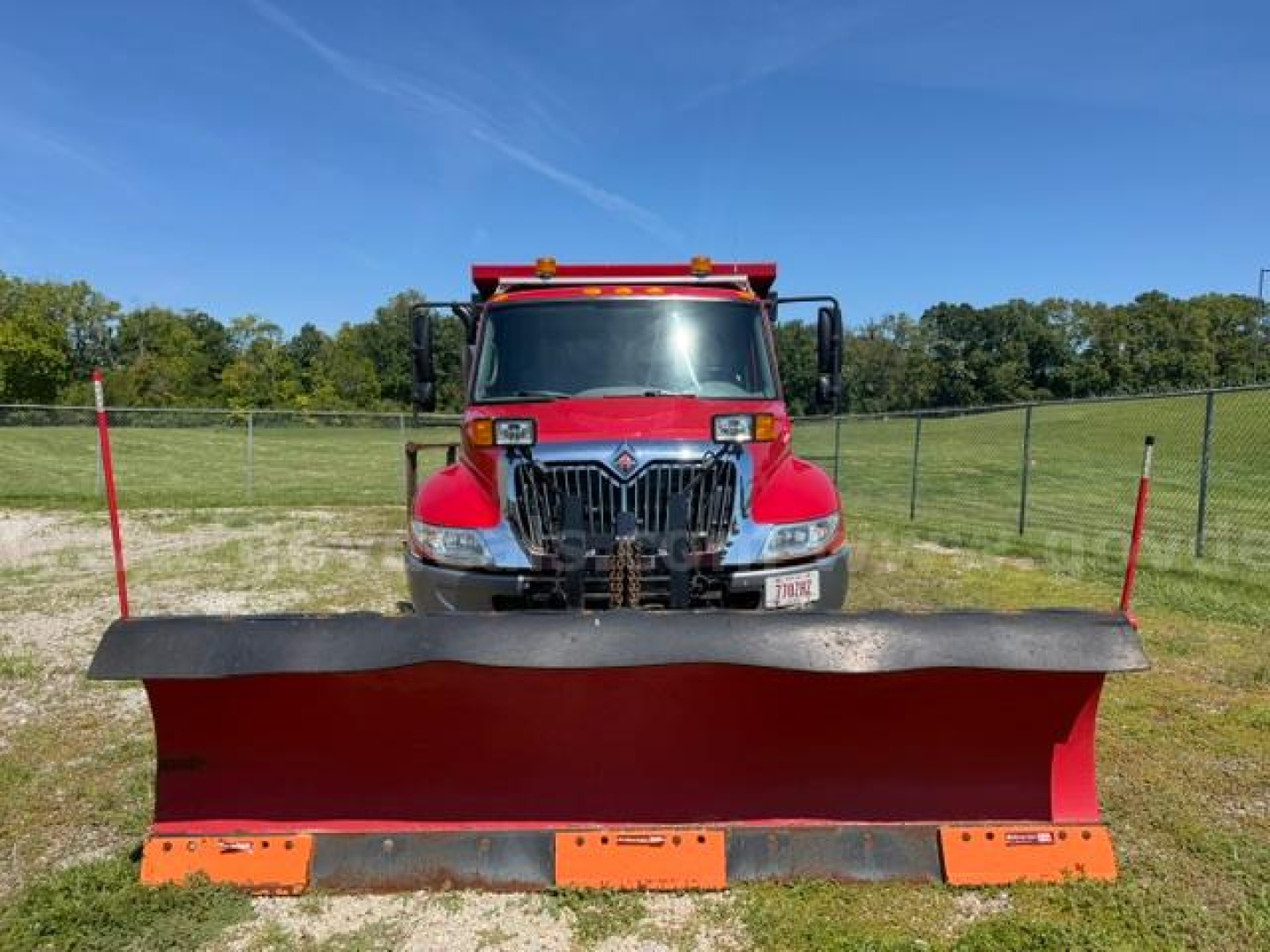 Heavy-duty white-cab international truck with a red plow attached front, large grille, headlights, and side mirrors in an open field.
