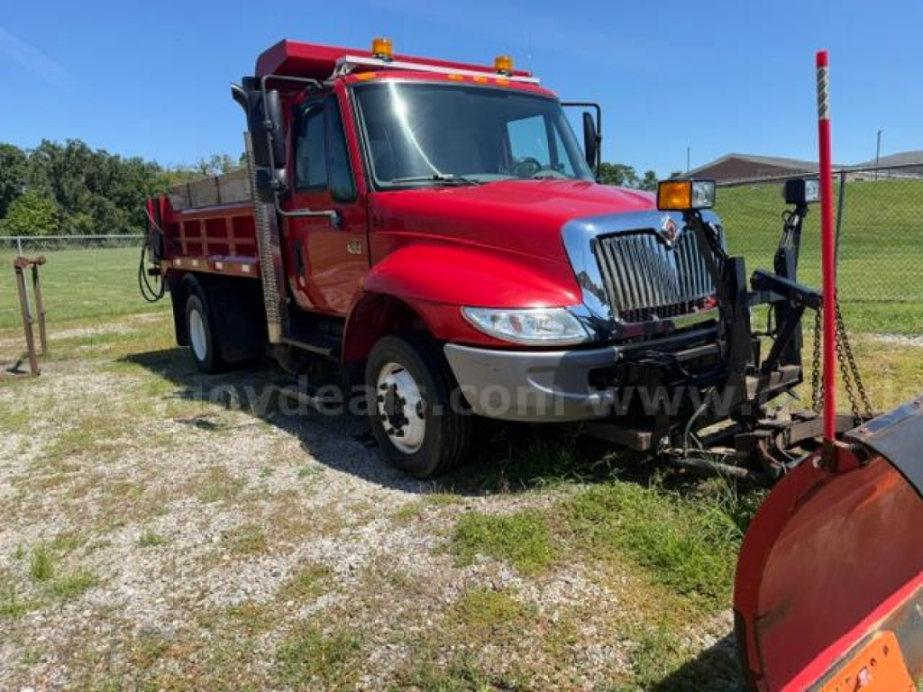 International 4300 plow truck side view showing red body, chrome grille, front bumper, and plow equipment attached.