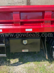Rear view of a red 2007 International 4300 truck showing a black toolbox mounted under the bed with a small emblem and label.