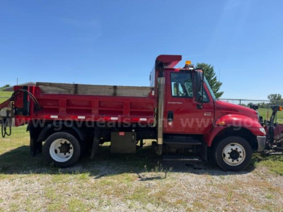Side view of a red International 4300 dump truck with a long bed and plow equipment, showing wheels, cab, and dump bed.