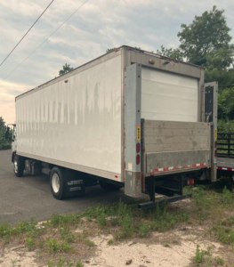 Kenworth reefer truck box rear view showing cargo trailer with liftgate and reflective tape. Visible text on side includes small white lettering near wheels and rear bumper area.