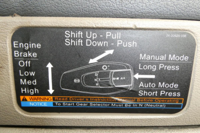 Cab interior label showing shift pattern diagram for manual and auto modes, with instructions: Shift Up - Pull, Shift Down - Push; Long Press Auto Mode, Short Press; warning notice about starting gear selector in Neutral; text includes Engi