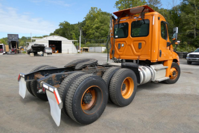 Truck chassis and cab of a 2017 Freightliner Cascadia 125 daycab with orange paint, rear triple-axle setup, visible fuel tanks, and chassis components.