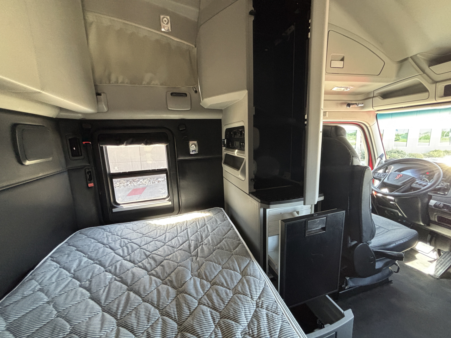 Kenworth T680 interior cab view showing sleeper bed, dashboard, and driver's seat with overhead cabinets and storage compartments.