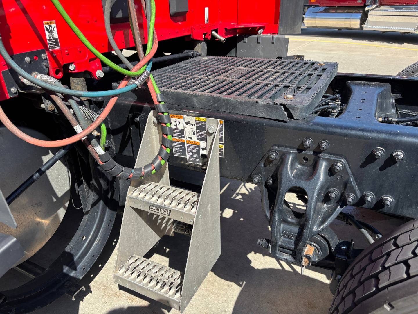 Kenworth T680 truck chassis showing a metal step with warning labels and exposed hydraulic lines near the catwalk and rear drive area.