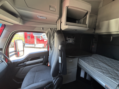 Kenworth T680 sleeper cab interior with bunk bed visible, captain seat facing forward, overhead storage shelves, and window close-up.