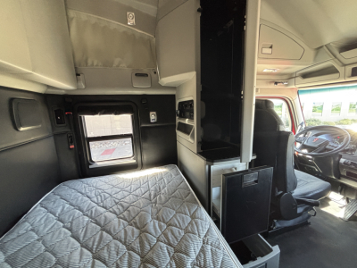 Kenworth T680 interior cab view showing sleeper bed, dashboard, and driver's seat with overhead cabinets and storage compartments.