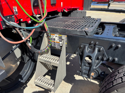 Kenworth T680 truck chassis showing a metal step with warning labels and exposed hydraulic lines near the catwalk and rear drive area.
