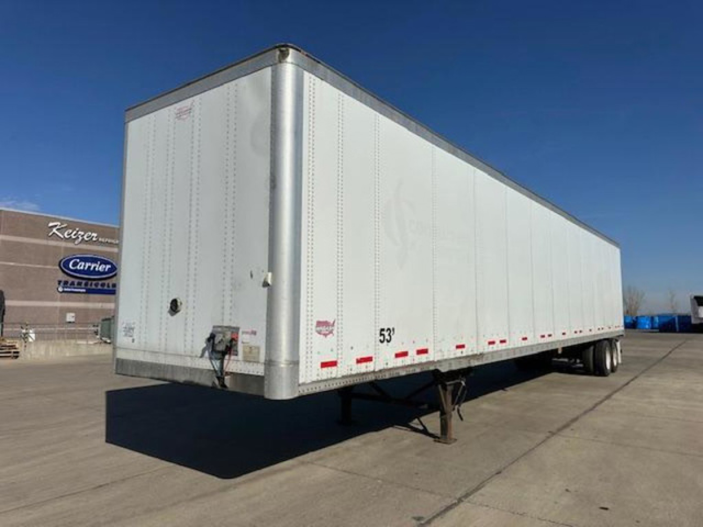 Trailer side view showing 53' box, white aluminum exterior, rear doors, leg stand, and dual rear axles.