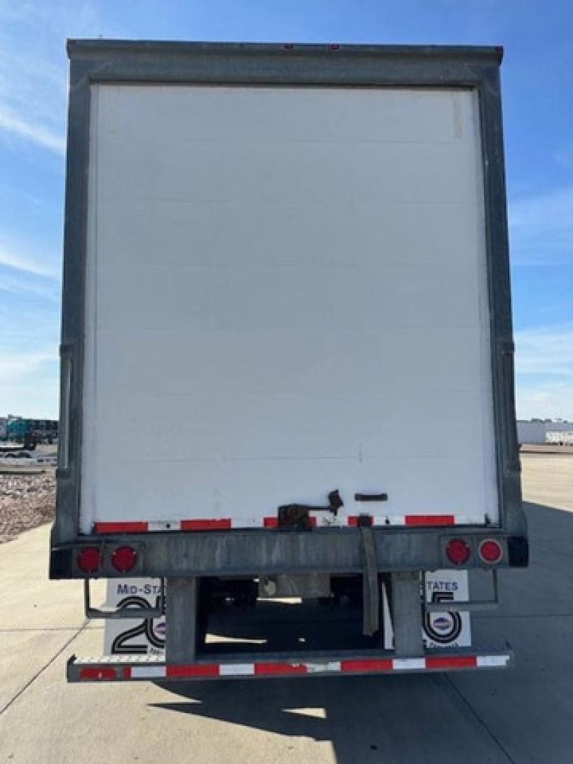 Rear view of a white Wabash van trailer with metal frame, red/white reflective striping, and bumper lights.