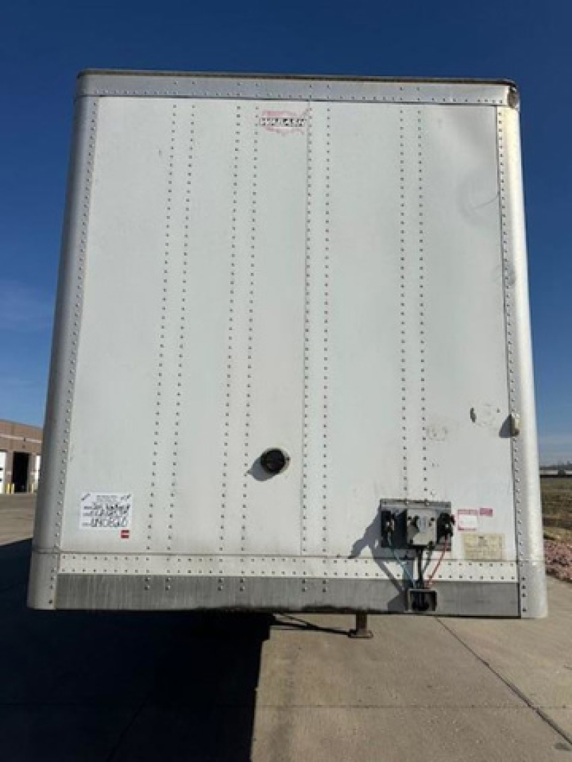 Rear view of a white Wabash van trailer showing doors, lights, and hitch area with various labels.