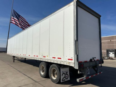 2014 Wabash trailer side and rear showing white box body with dual rear axles, United States flag in background.