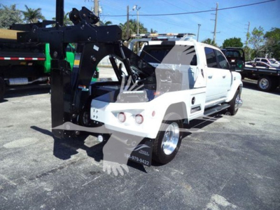 Ram pickup truck with winch equipment attached in front, white body, black winch crane and hook assembly, at a dealership lot.