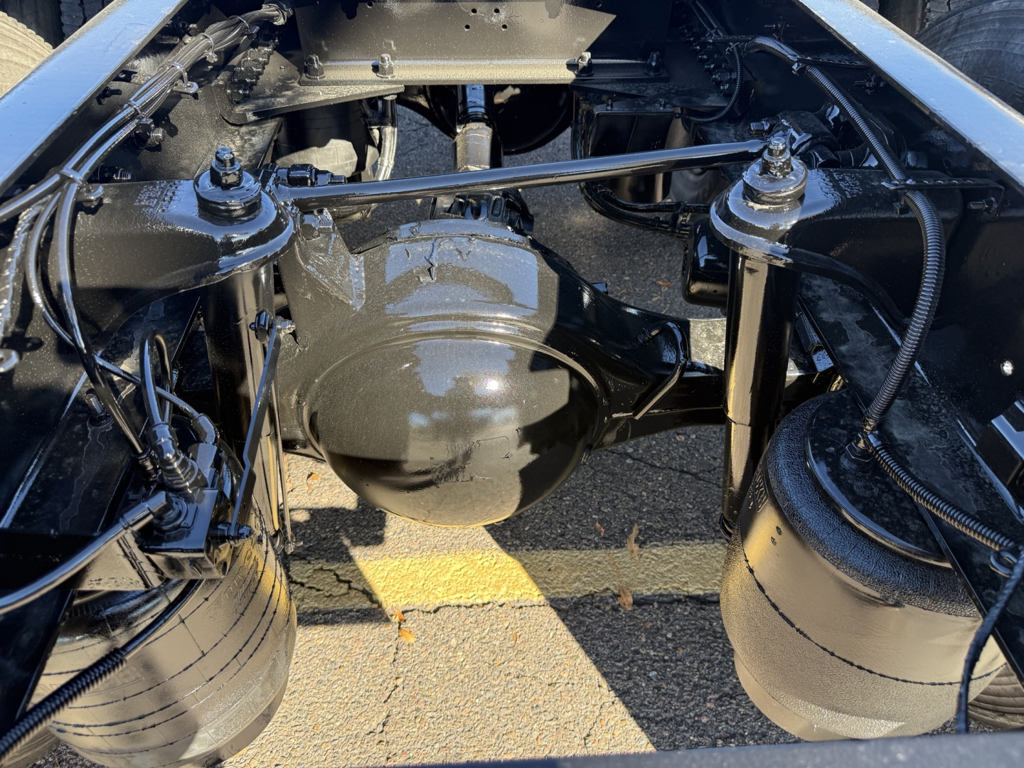 Kenworth T880 chassis view showing front axle housing and air suspension bags, with brake lines and wiring visible.