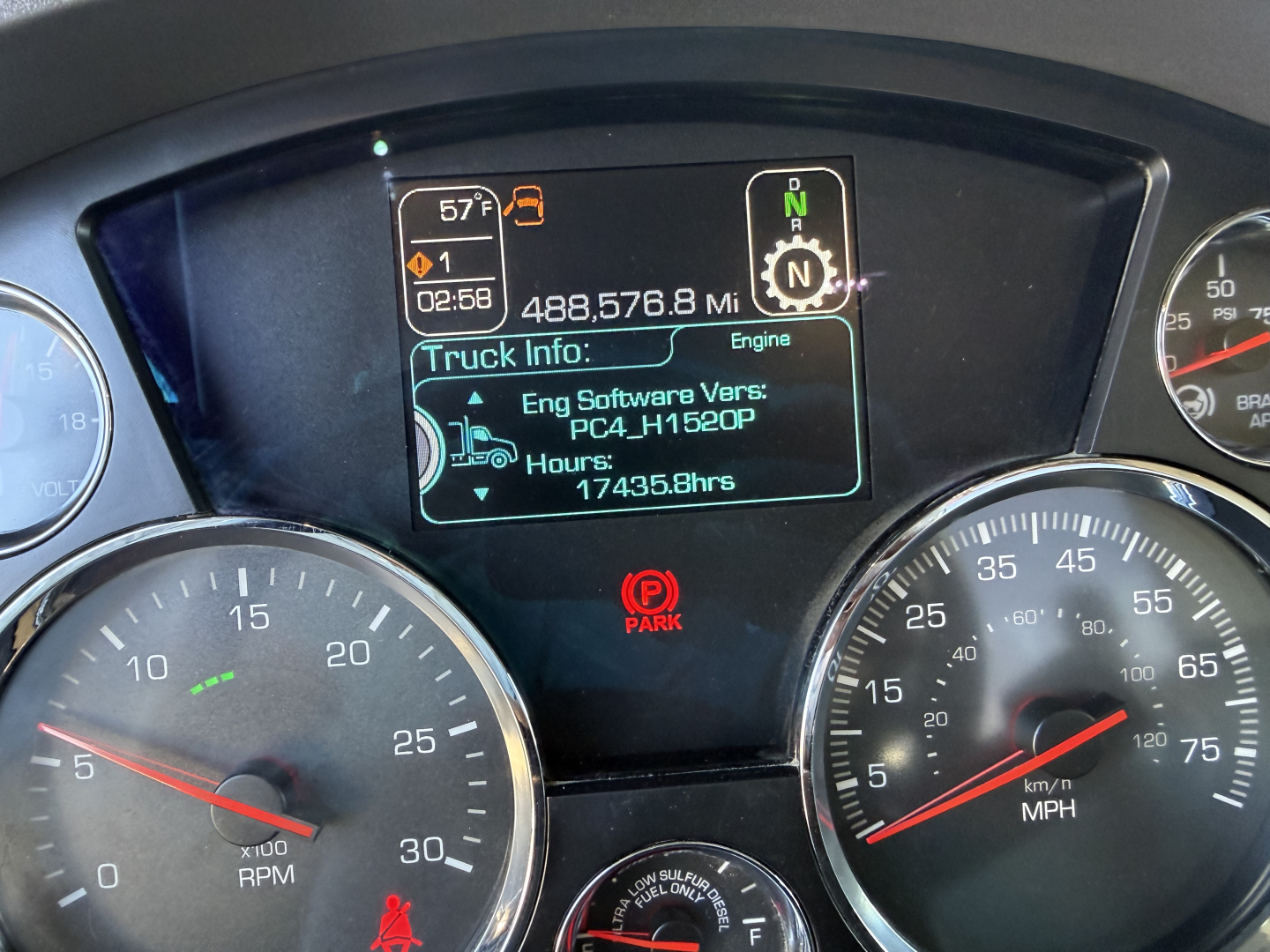 Kenworth T880 instrument cluster showing digital display with truck hours and engine software version; RPM gauge left, speedometer right, rearview parking indicator in center.