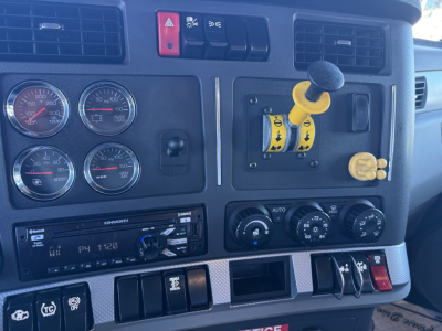Vehicle dashboard of a 2020 Kenworth T880 showing steering column with yellow gear selector, four gauges, lightweight controls, and Kenworth radio head unit.