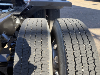 Kenworth T880 rear dual wheels showing tread and axle area; visible are two front dual tires, part of truck chassis, with wheel hubs and suspension components.