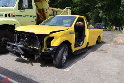 2016 Ford F-150 pickup truck damaged front end with open driver door in yellow, tow bed behind, in a lot.