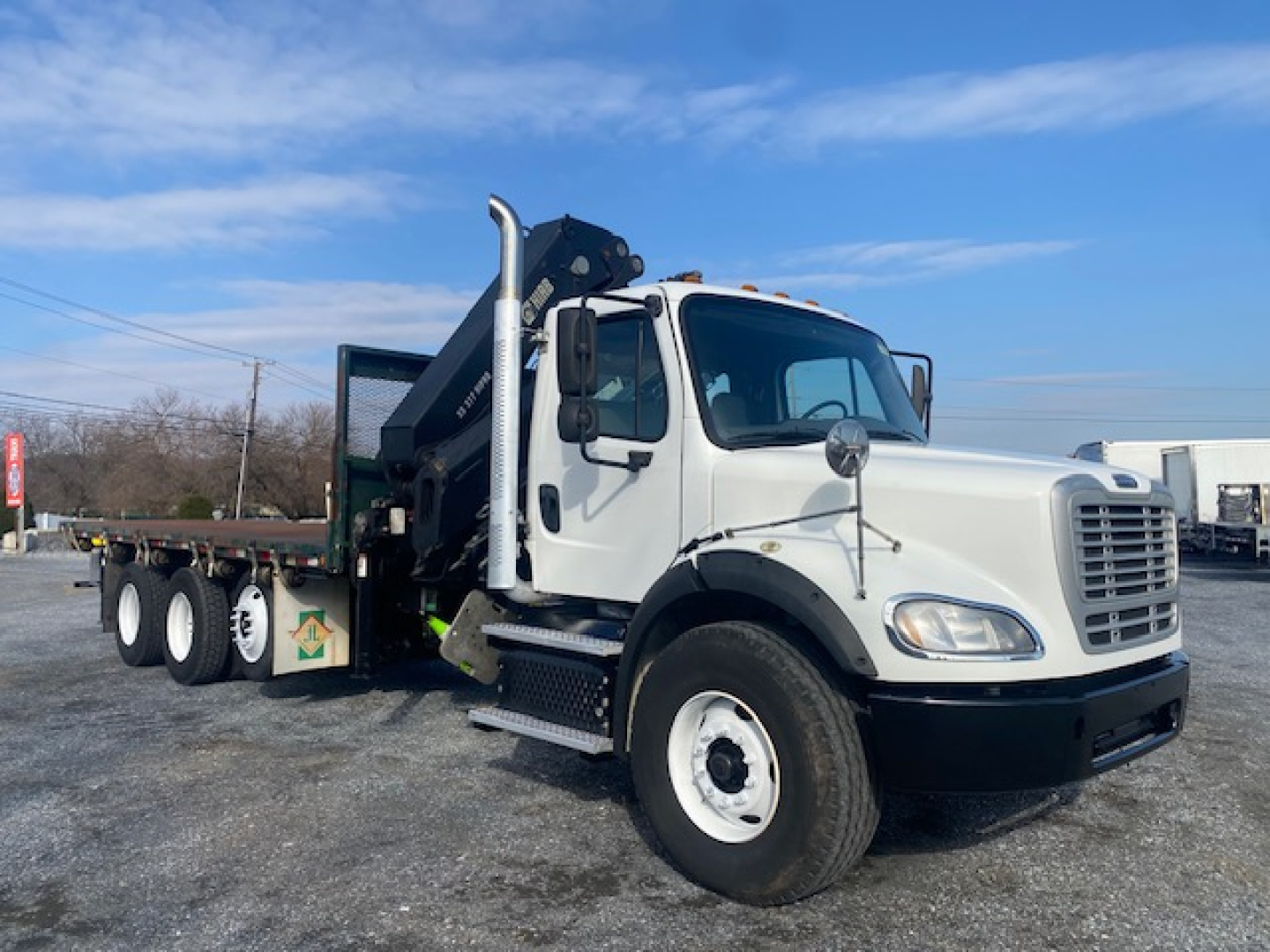 Truck cab with crane mounted on flatbed, Freightliner M2-112 style, white cab, black bumper, crane arm folded by the cab.