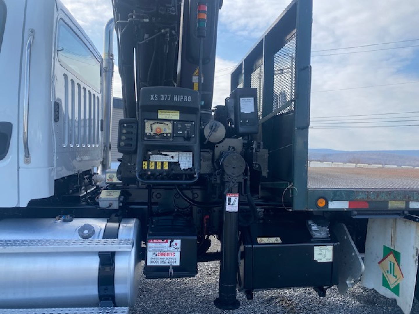 Crane-equipped Freightliner M2-112 truck side view showing crane controls and operator platform with labels and warning decals.