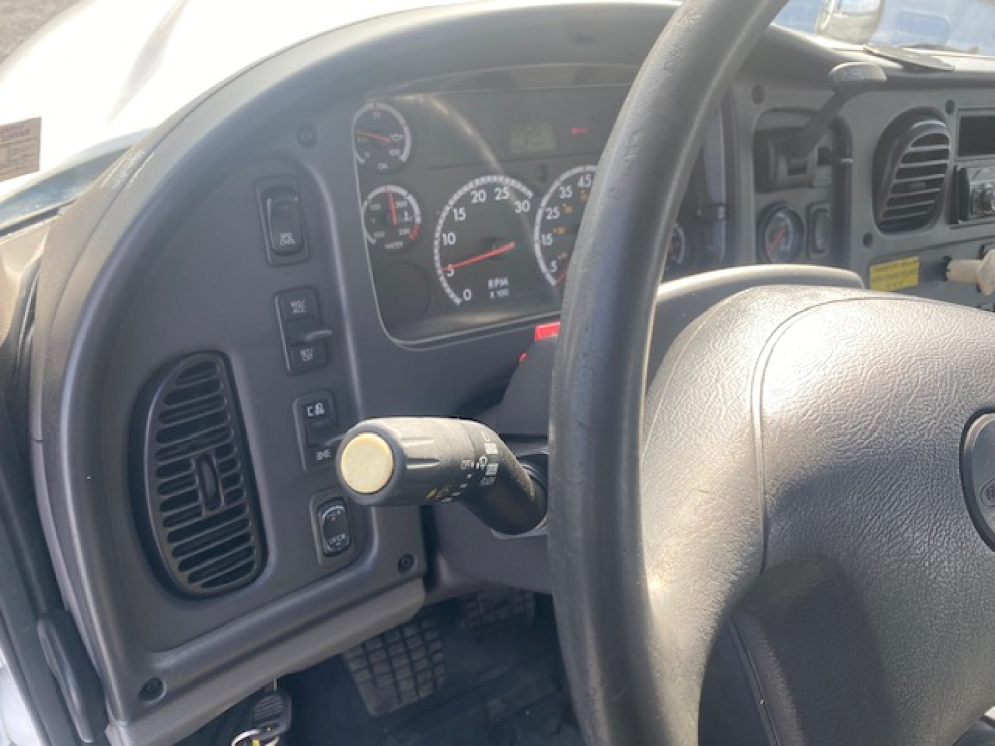 Dashboard and steering wheel of a Freightliner M2-112 crane truck showing gauge cluster and control stalks.
