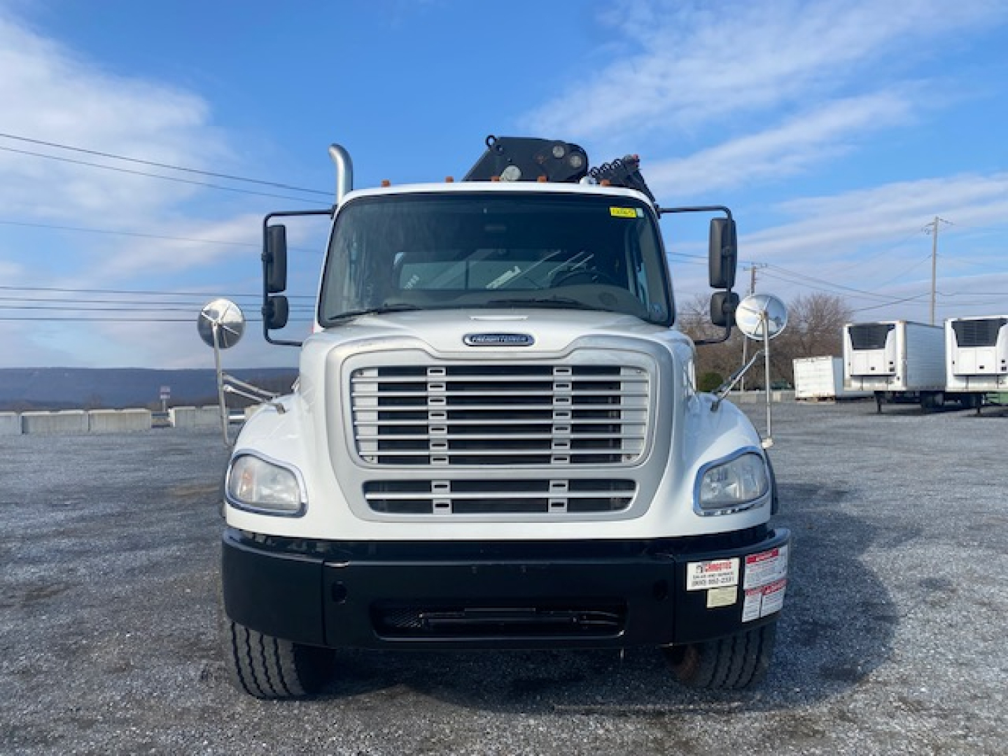 Front view of a Freightliner M2-112 crane truck showing large grille, rectangular headlights, mirrors, and a crane apparatus on top.